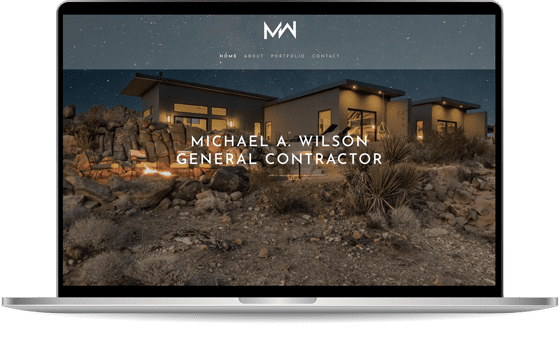 A laptop displaying a website for Michael A. Wilson, General Contractor, featuring a modern house in a rocky, desert landscape. The website has navigation links for Home, About, Portfolio, and Contact.