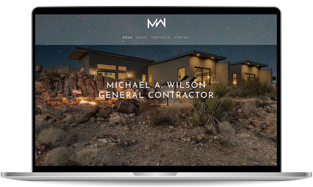 A laptop screen displaying a website for Michael A. Wilson, General Contractor, featuring a modern house at dusk in a rocky, desert landscape.